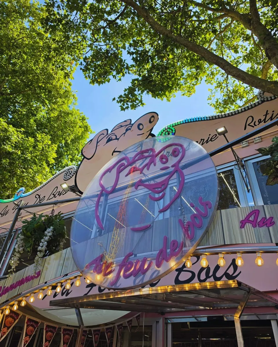Enseigne néon rose en forme de tête de cochon portant la mention Au feu de bois, photographiée en contre-plongée sur fond de ciel bleu
