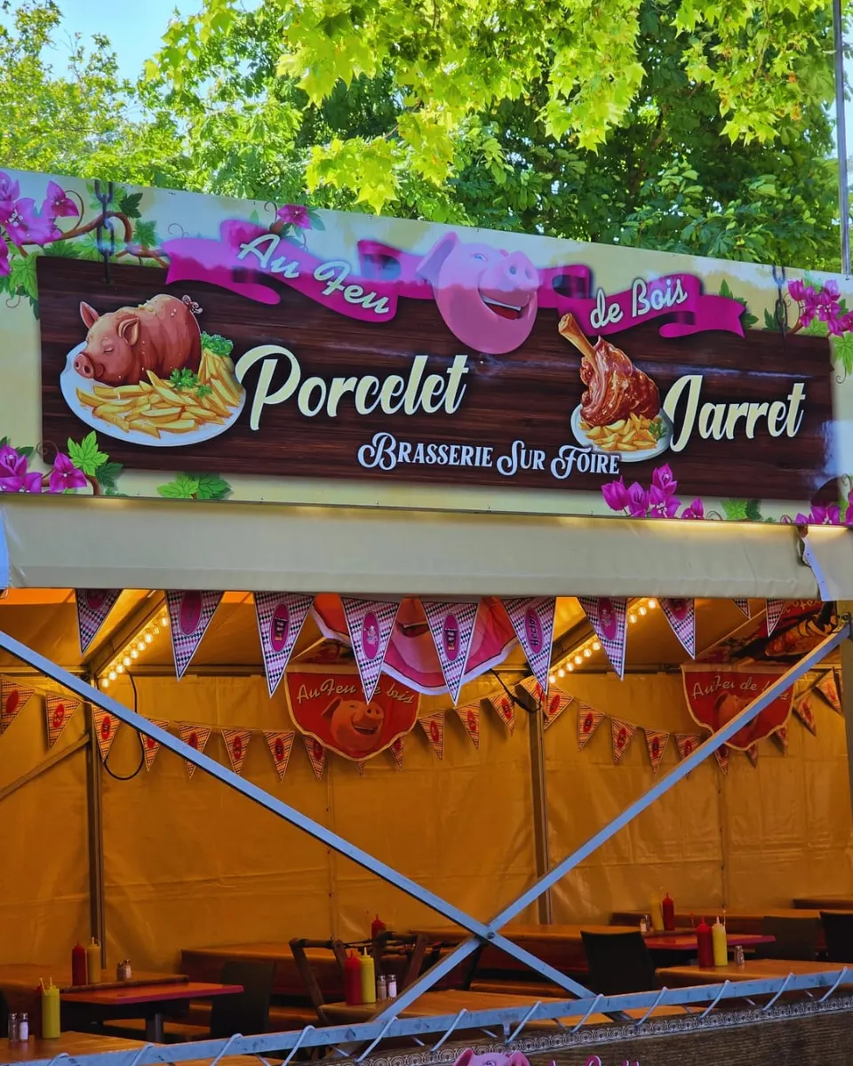 Enseigne peinte Au Feu de Bois avec un cochon rose souriant, les mots Porcelet et Jarret, au dessus d'une salle décorée de fanions roses