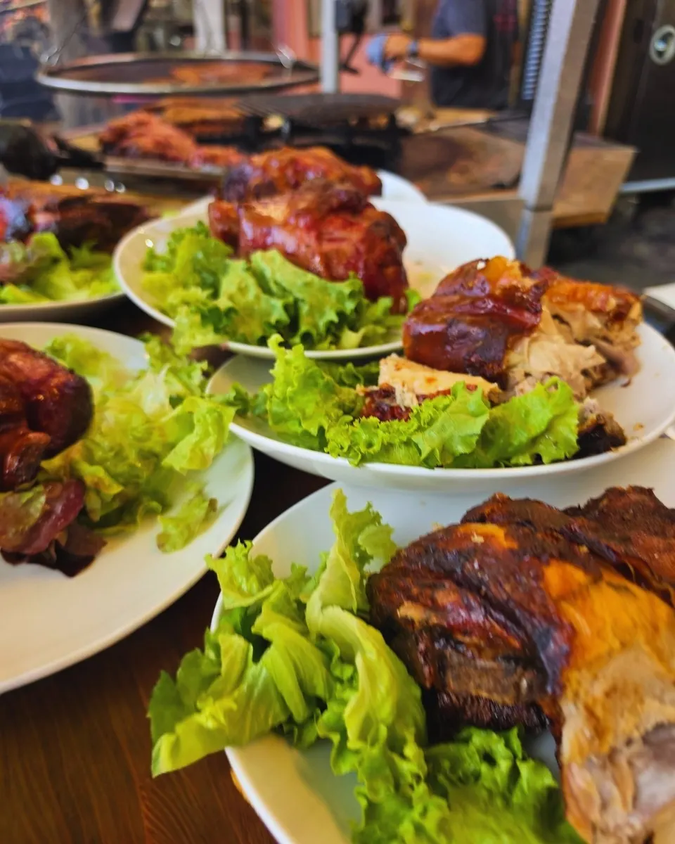 Assiettes de jarret grillé sur lit de salade alignées sur la table en bois, prêtes à être servies.