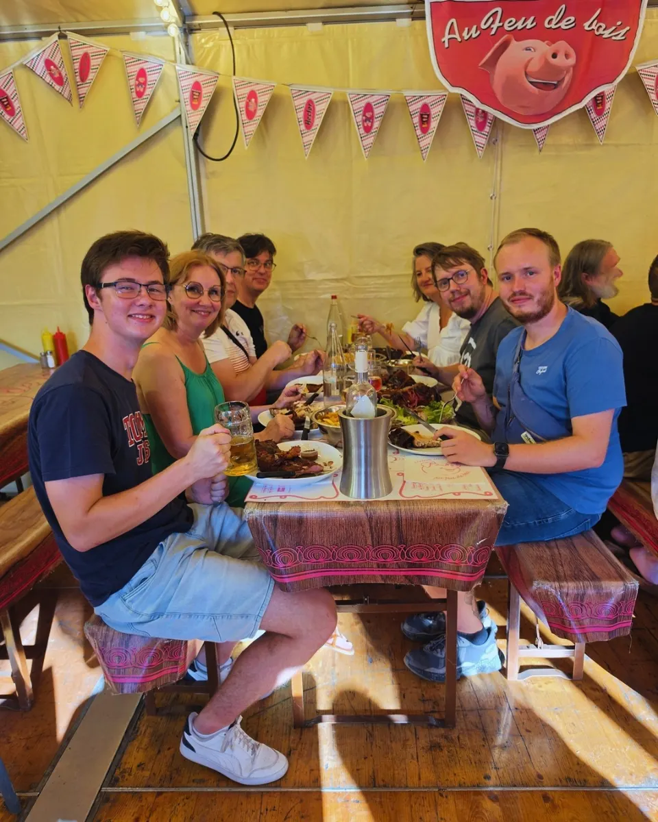 Six convives souriants attablés sous le chapiteau devant des assiettes de viande grillée, sous le blason du cochon Au Feu de bois