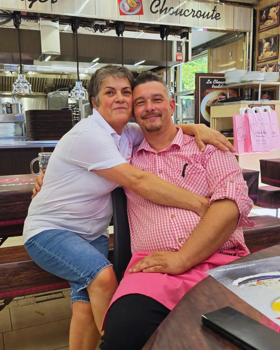 Le duo de patrons enlacés dans la cuisine du stand, entre sacs roses au logo cochon et affiches de la maison.