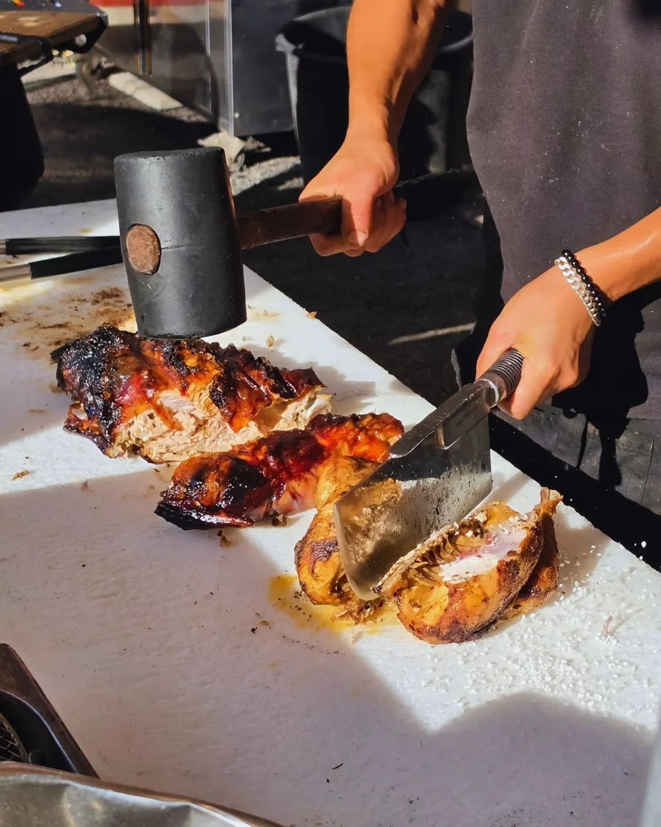 Mains tranchant au couperet des morceaux de cochon grillé à la peau croustillante, en plein soleil.