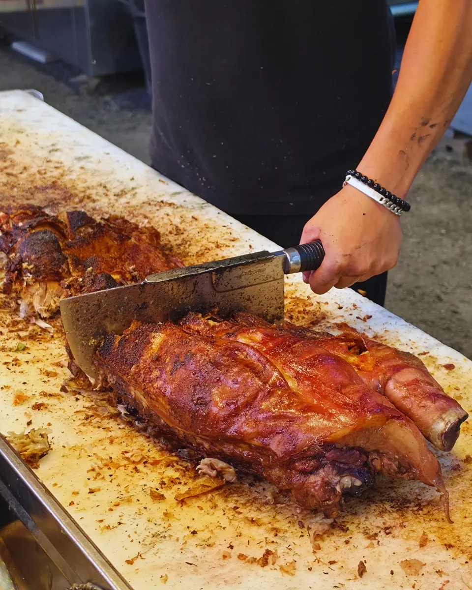 Gros plan sur la découpe au couperet d'une pièce de cochon rôti à la couenne caramélisée.