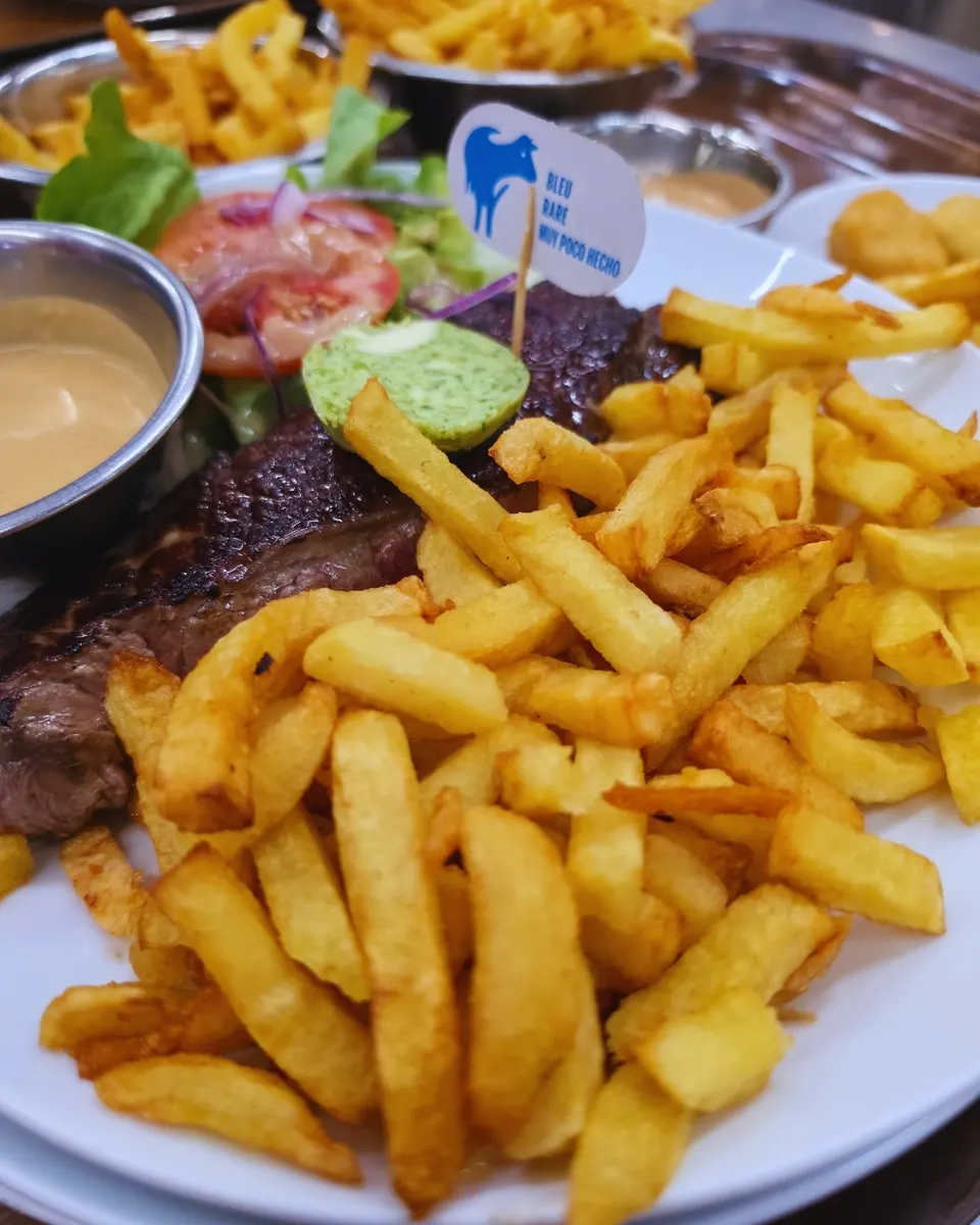 Entrecôte grillée au beurre persillé, frites maison, salade tomate-oignon et sauce au poivre.