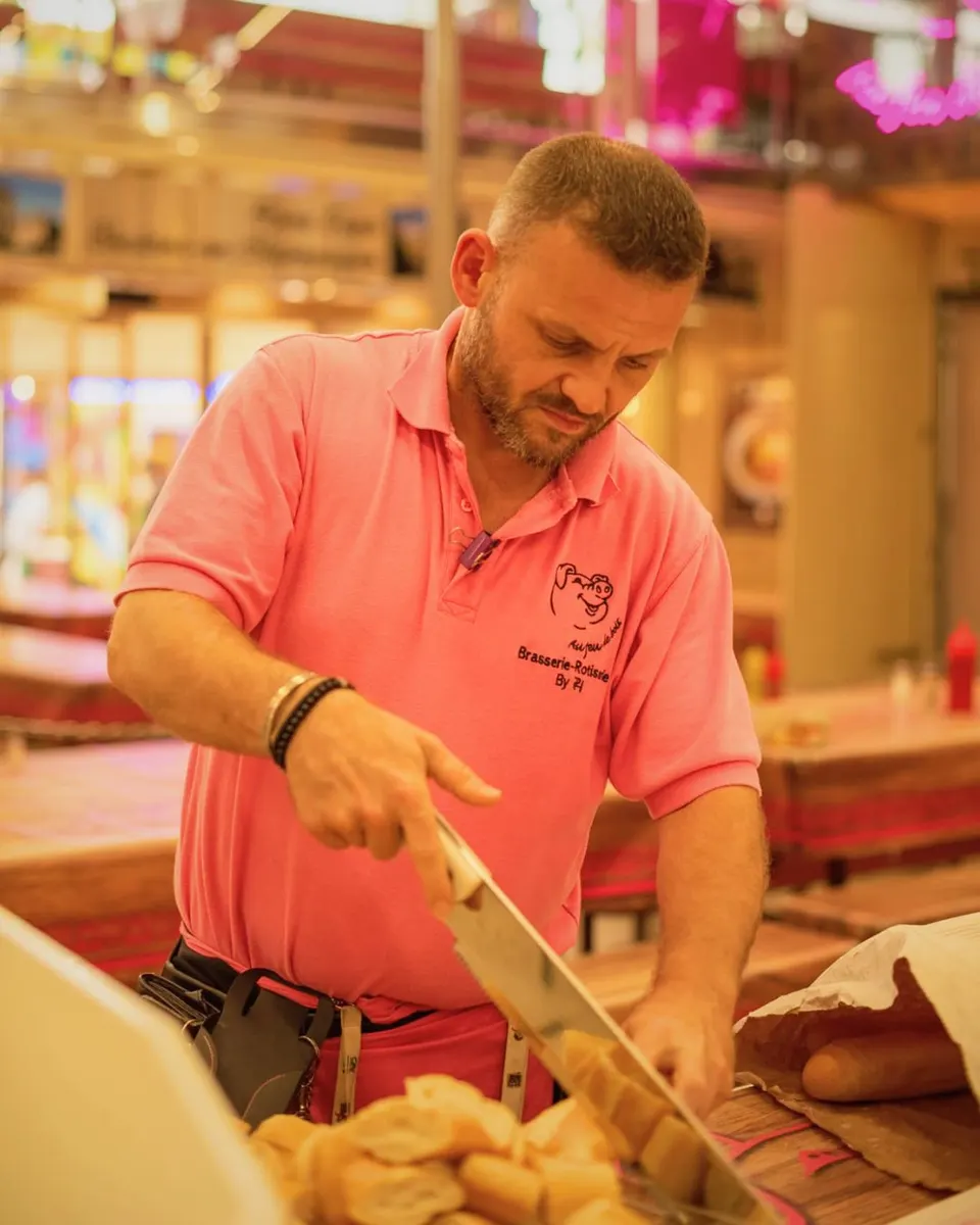 Homme en polo rose tranchant des baguettes de pain au grand couteau sur une planche à découper