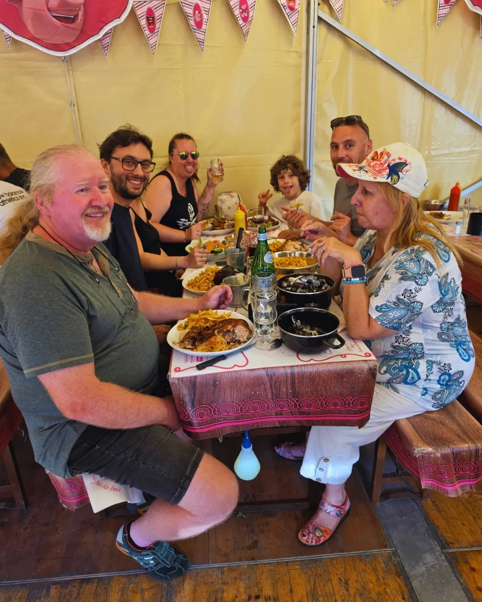 Famille attablée sous le chapiteau devant cochon grillé, frites et cocottes de moules sur les sets Au Feu de Bois.