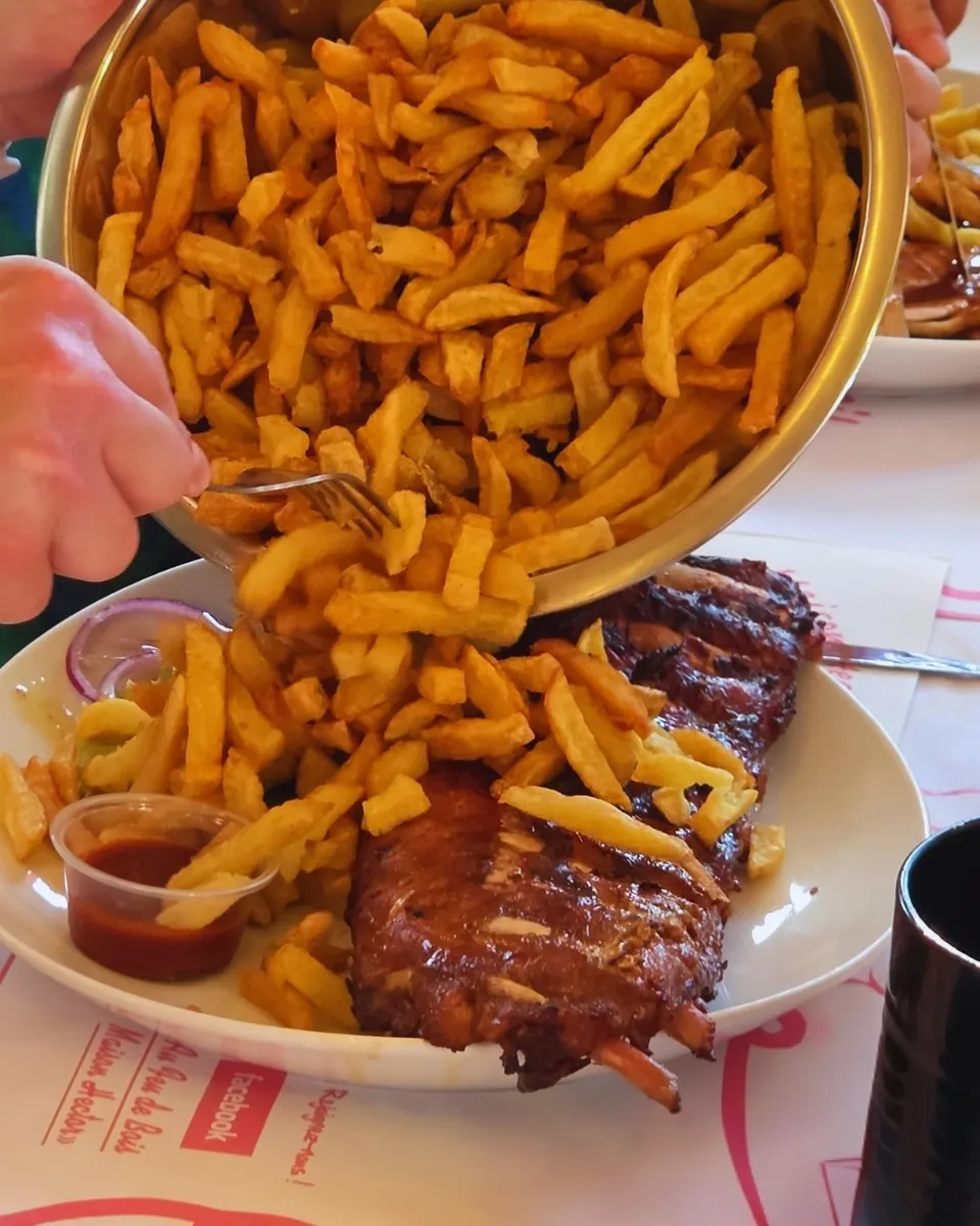 Frites maison versées en cascade sur une assiette de travers de porc laqué, nappe au logo Maison Hector.