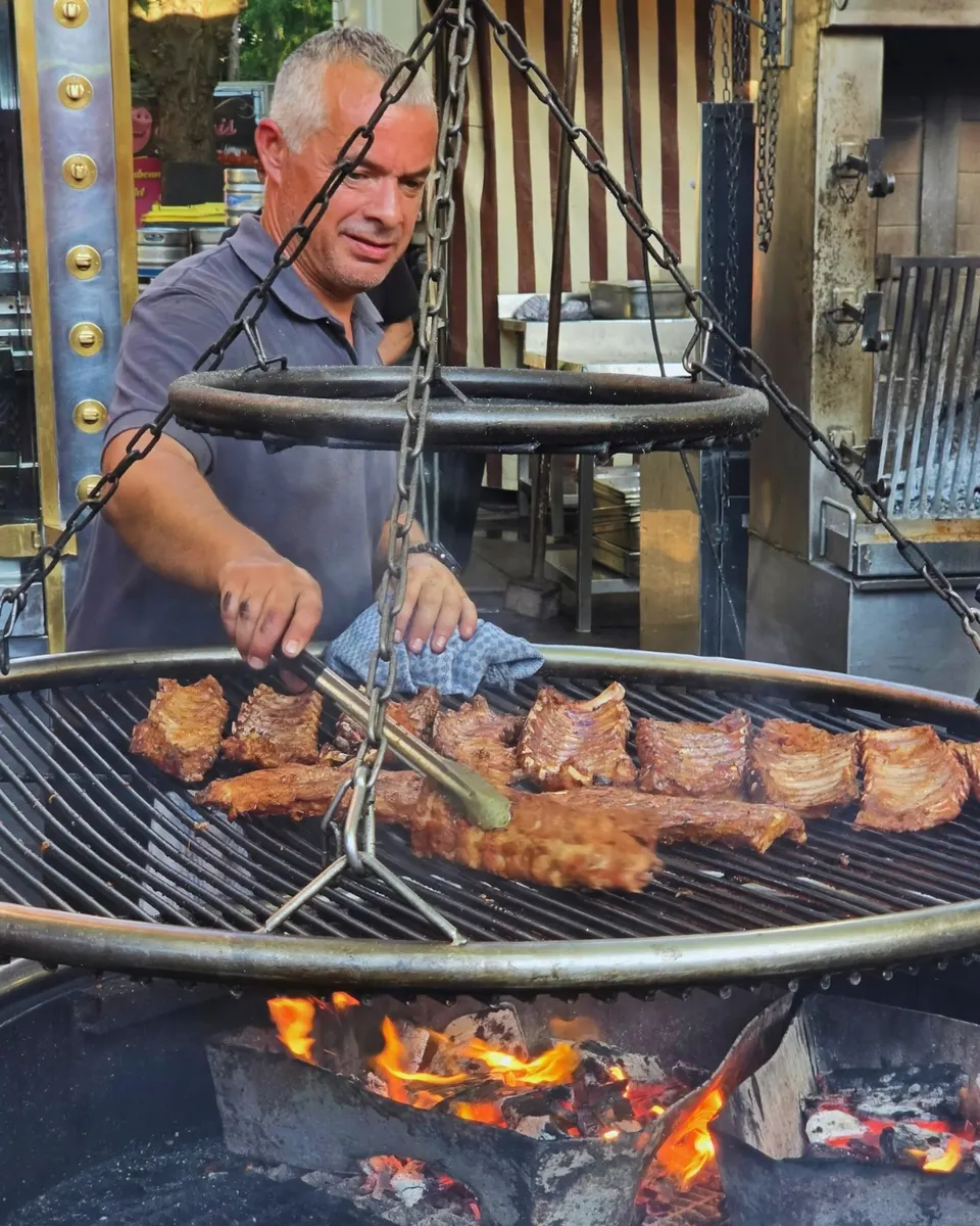 Un rôtisseur surveille la grille suspendue au-dessus des flammes du feu de bois