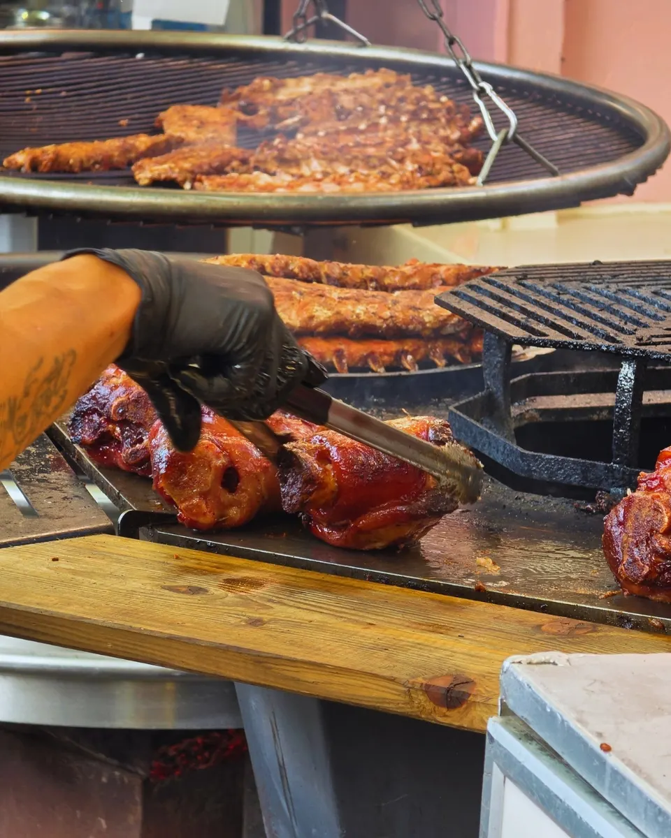 Jarrets de porc caramélisés saisis à la pince sur la plancha, sous une grille ronde chargée de travers.