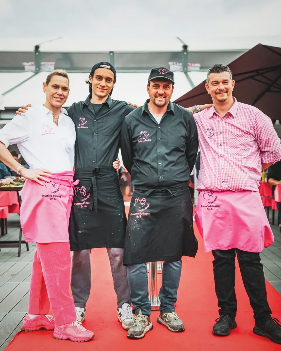 Les patrons de la Maison Hector posant ensemble en tenue de service, tabliers roses et chemises brodées du cochon