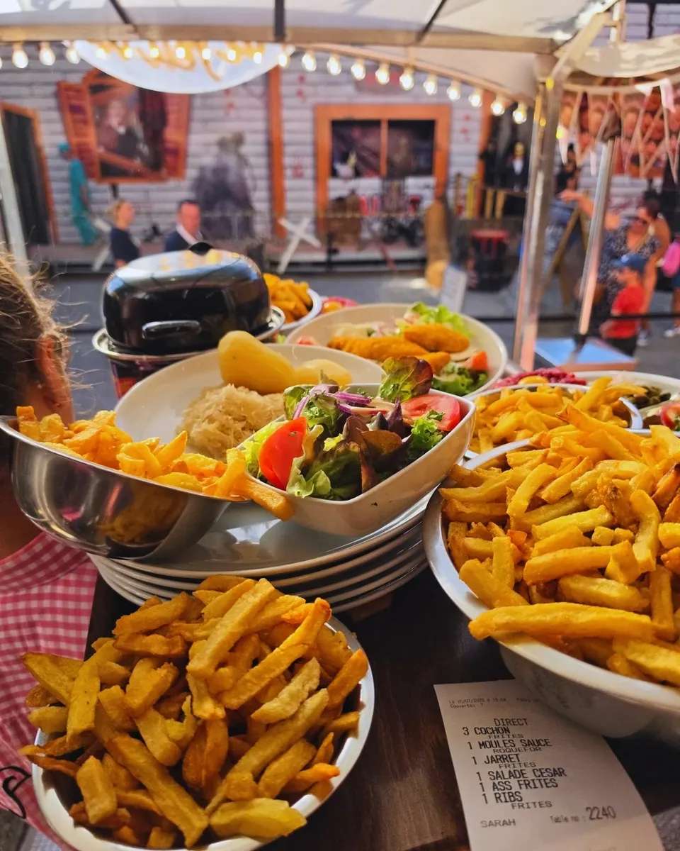 Plateau de service chargé d'assiettes de frites, salades et choucroute, ticket de commande au premier plan.