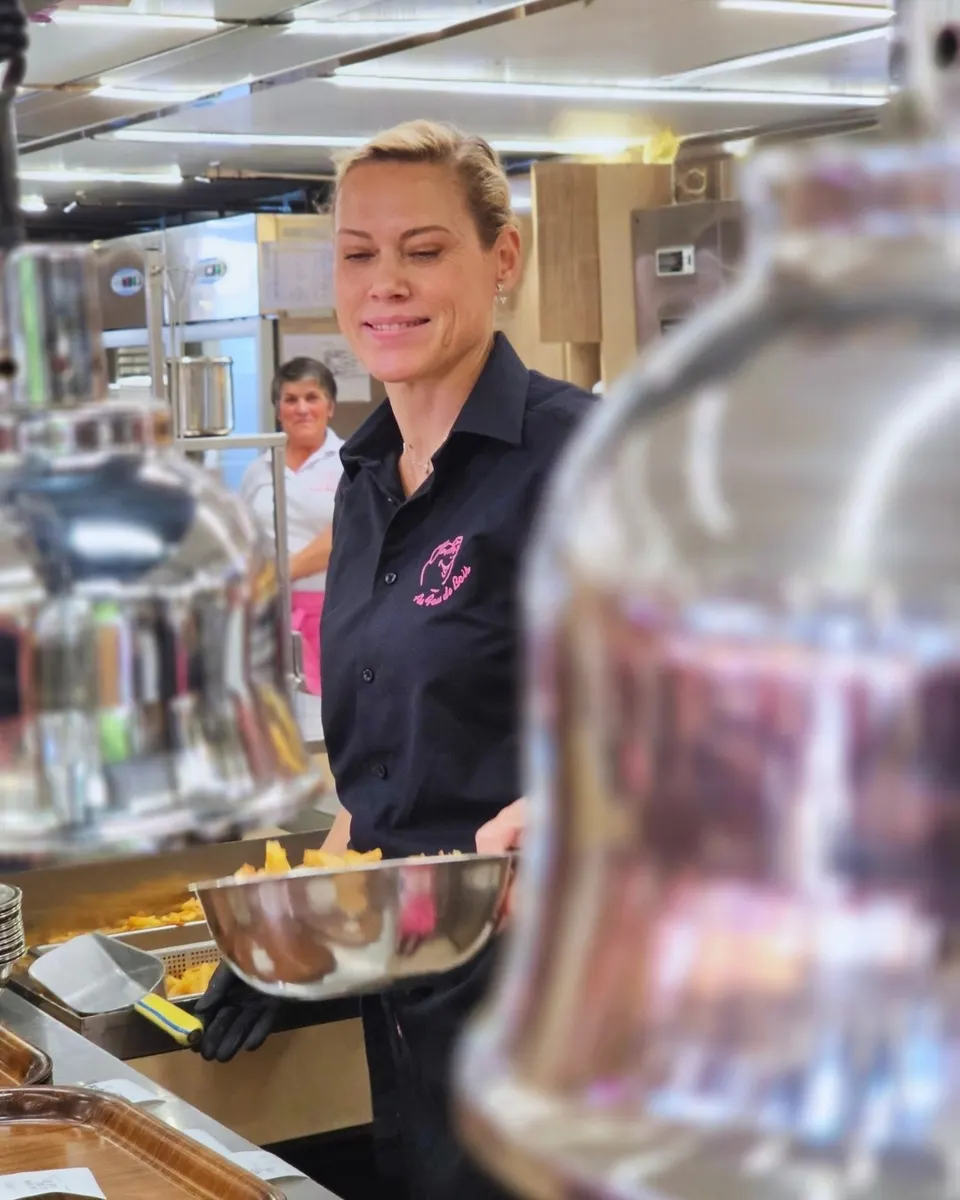 Portrait souriant d'une employée en chemise noire brodée du cochon rose, saladier de frites en main.