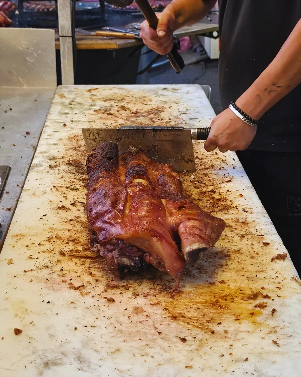 Le rôtisseur en pleine action, couperet planté dans la pièce de cochon rôti devant les grills.
