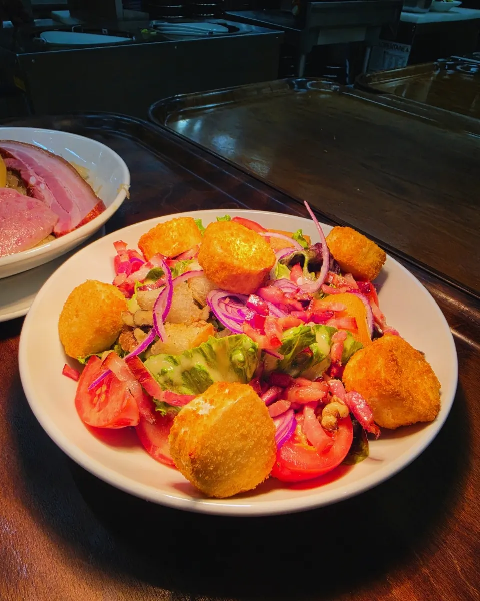 Salade au chèvre chaud pané, lardons et noix dans une chaude lumière d'ambiance.