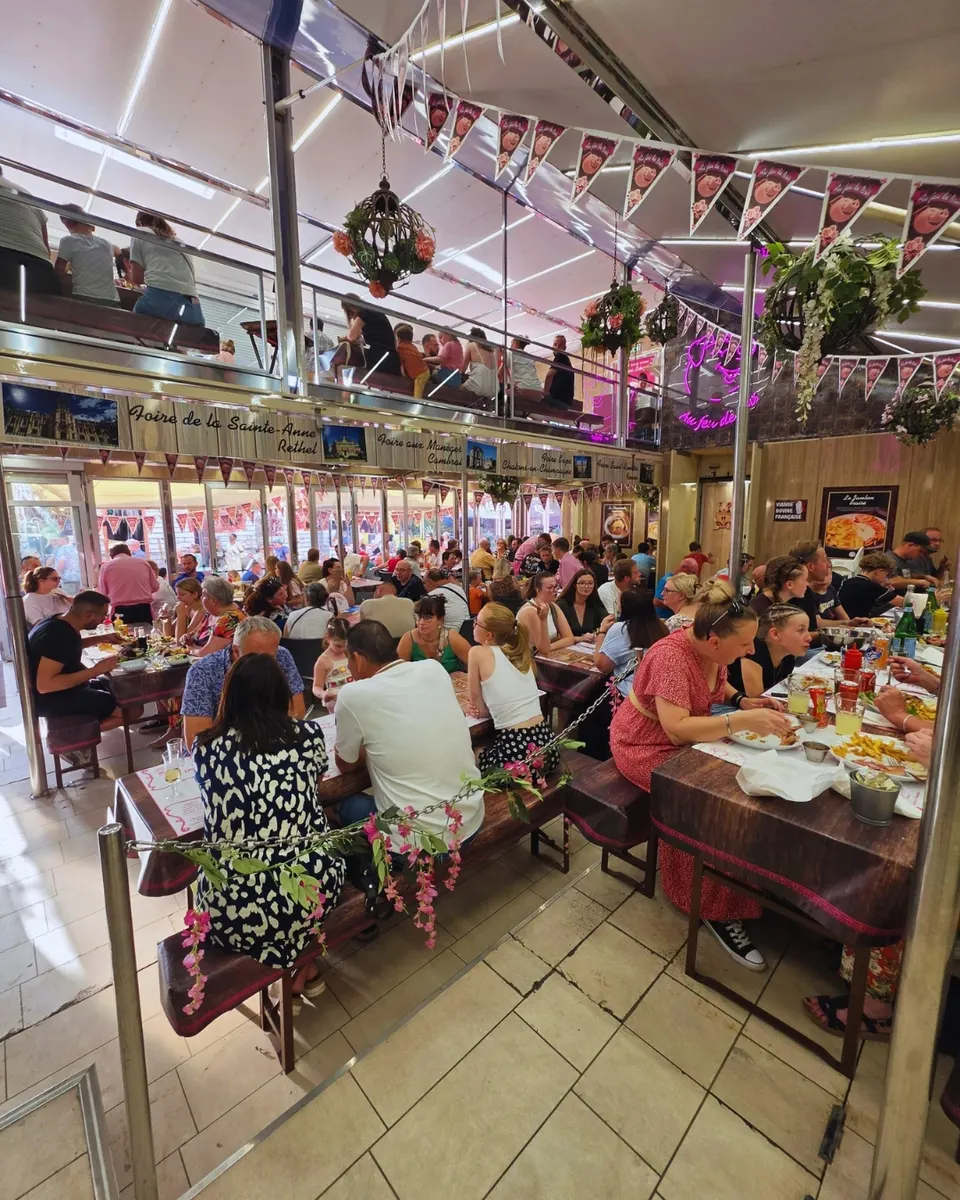 Vue intérieure du restaurant éphémère bondé, longues tables en bois, fanions et néon rose au cochon mascotte.