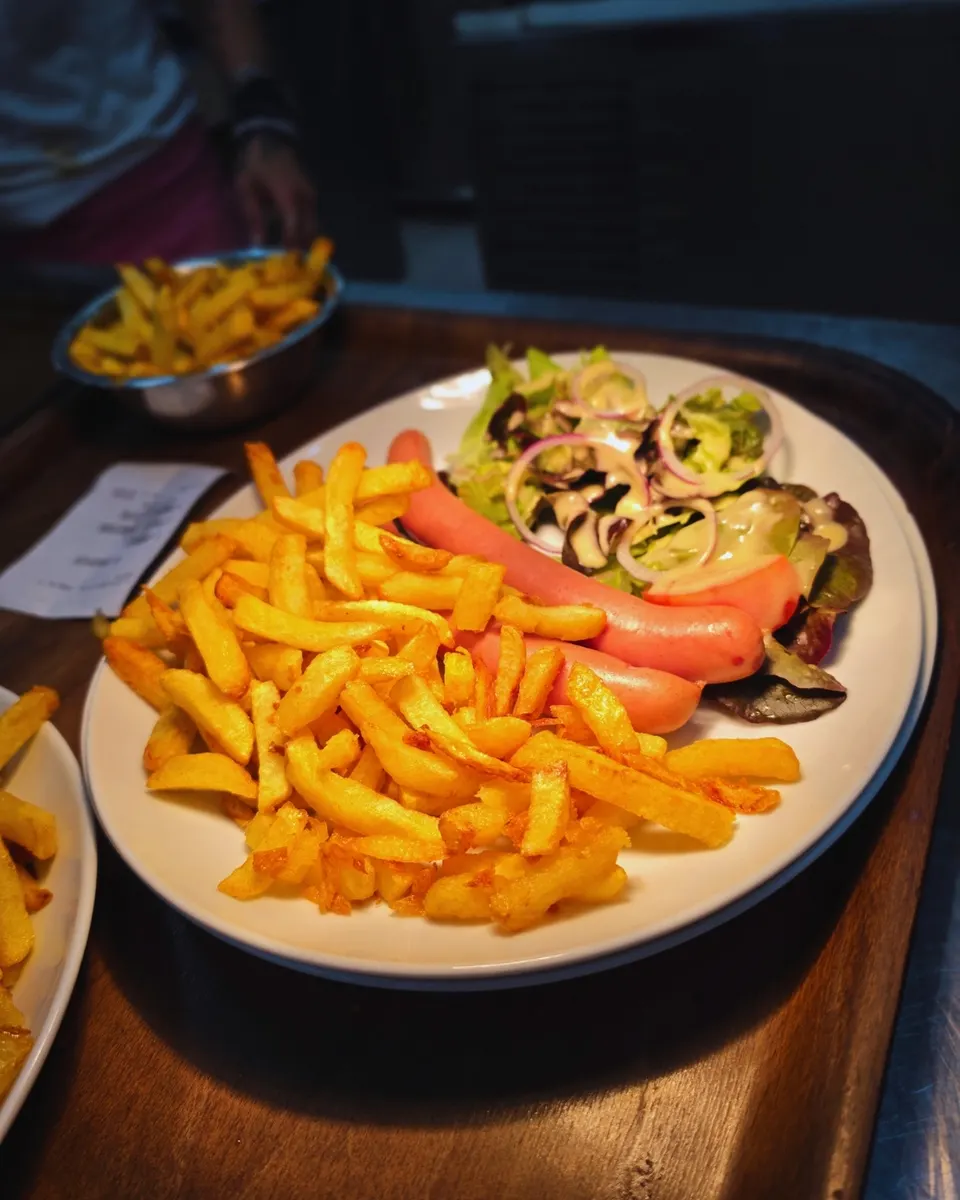 Assiette de saucisses sur lit de salade aux oignons rouges avec une grosse portion de frites dorées.