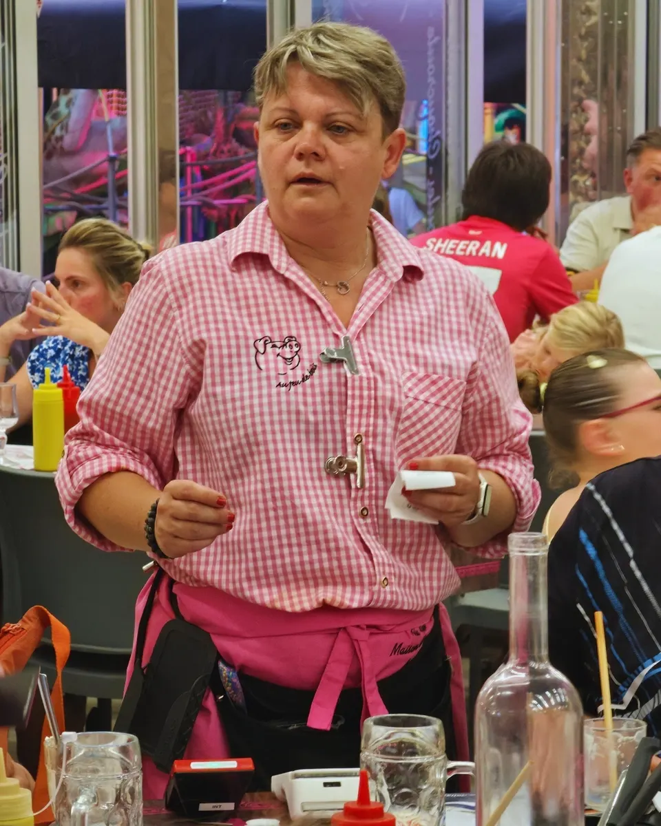 Serveuse prenant une commande, chemise vichy rose au cochon brodé et tablier rose.