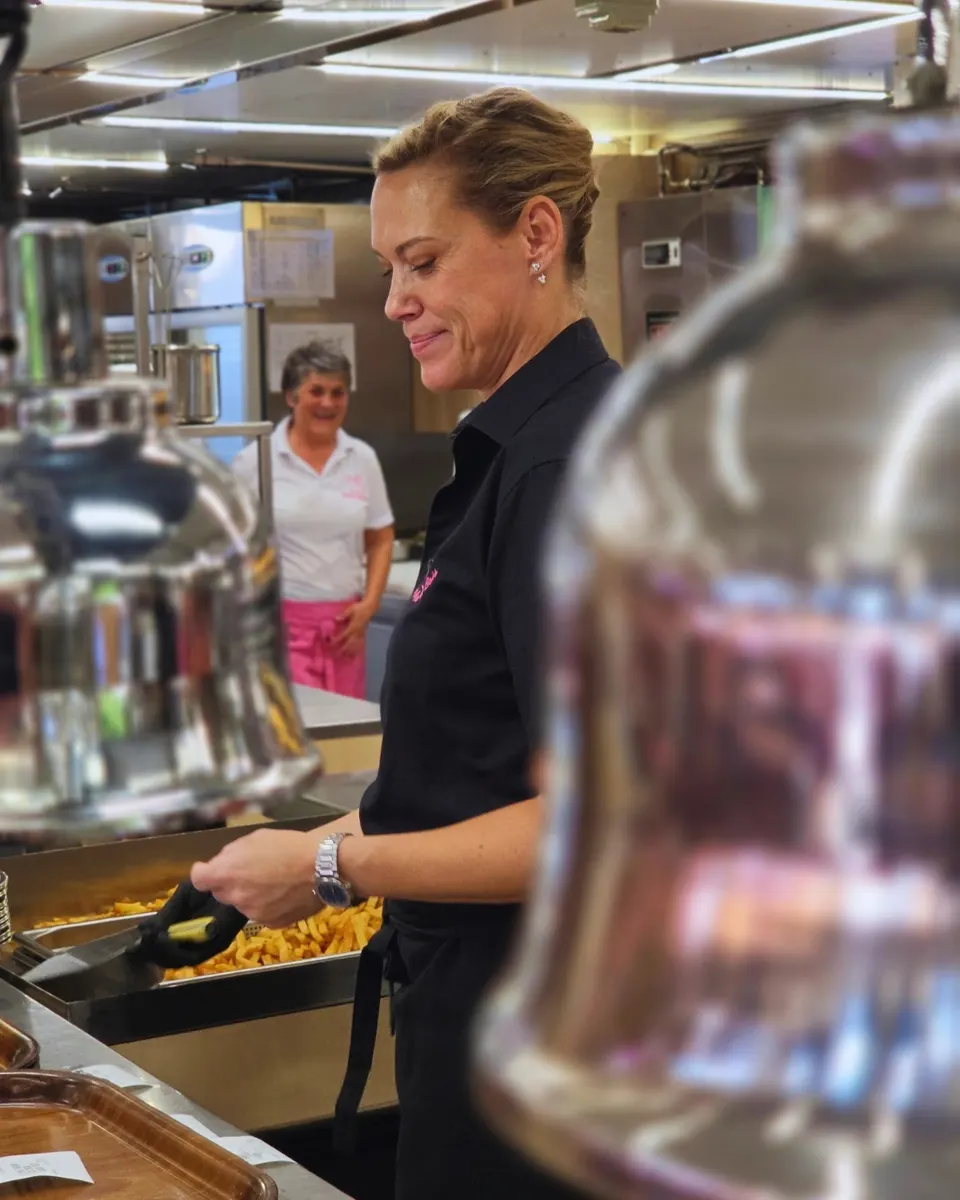 Employée souriante servant les frites à la pelle dans la cuisine du stand.