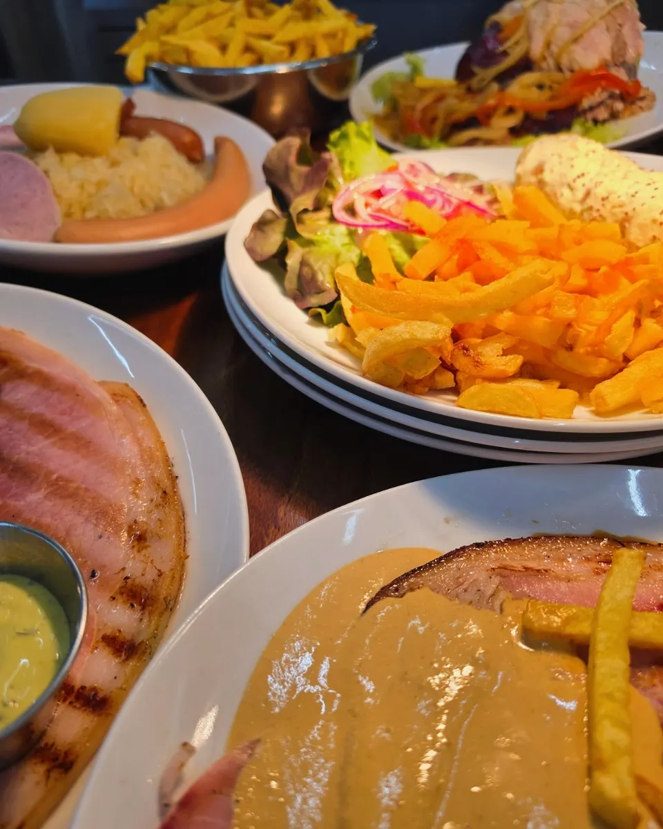 Tablée de plats de brasserie : choucroute garnie, frites maison, jambon grillé et viandes en sauce.
