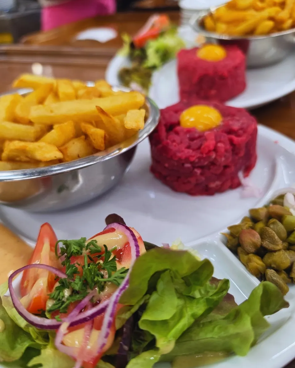 Travers de porc laqués et brillants empilés sur un plat inox devant la grille du feu de bois.
