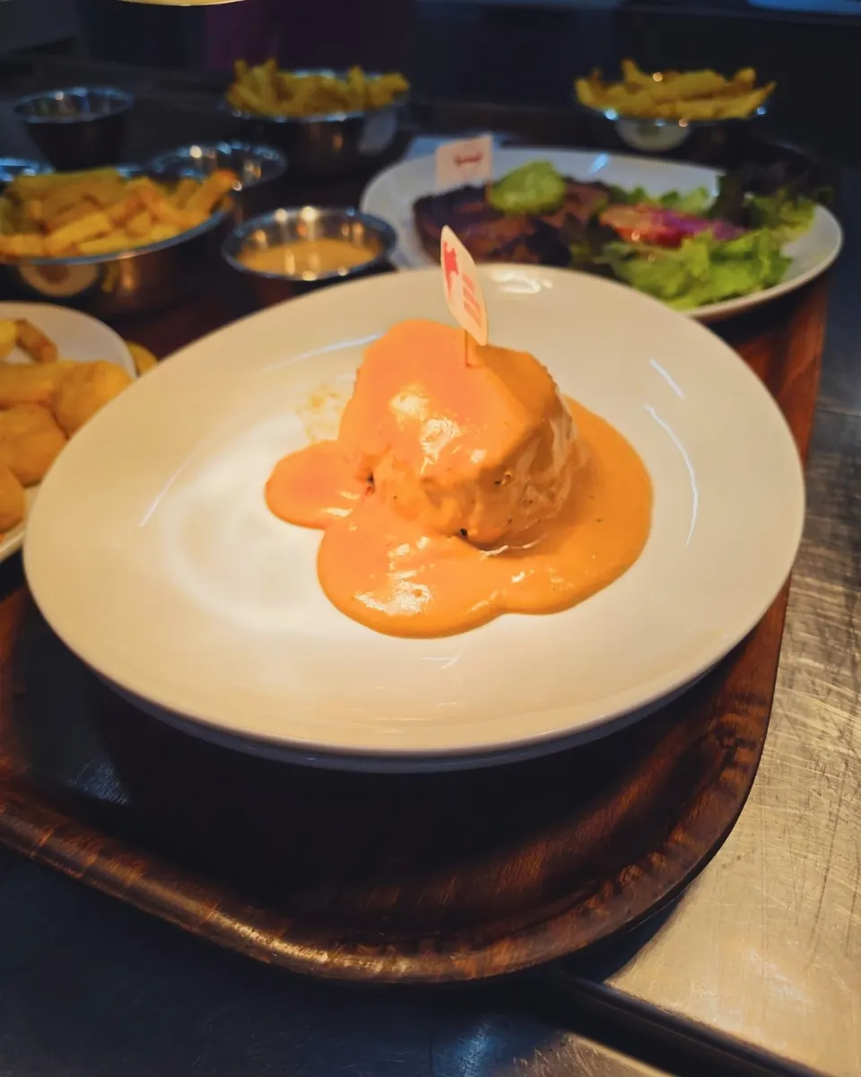 Pièce de viande en sauce sur plateau bois, entourée de frites et pommes dauphines.